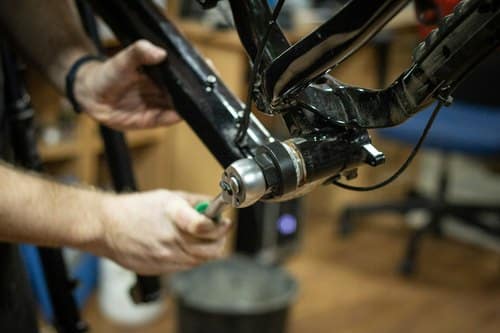 Werkzeug fürs Fahrrad: zwei Hände schrauben mit einem Werkzeug am Rahmen eines Fahrrads