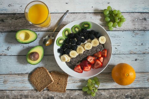 Gesunde Ernährung: Frühstücksschale mit Obst und Chiasamen, daneben Avocado und Vollkornbrot