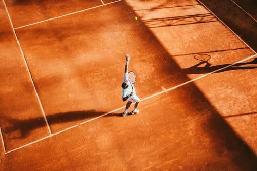 Tennisspieler beim Aufschlag auf einem Sandplatz, von oben fotografiert